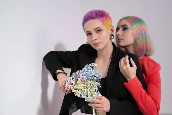 Mujer joven lesbiana pareja con pelo corto de colores vivos y chaquetas posando sobre fondo blanco. Piercing en la cara, túneles en las orejas. —  Fotos de Stock