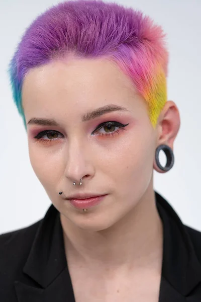 A young beautiful girl with short colored hair. Spread bright coloring and creative make-up. Piercing on the face. A black jacket. — Stock Photo, Image