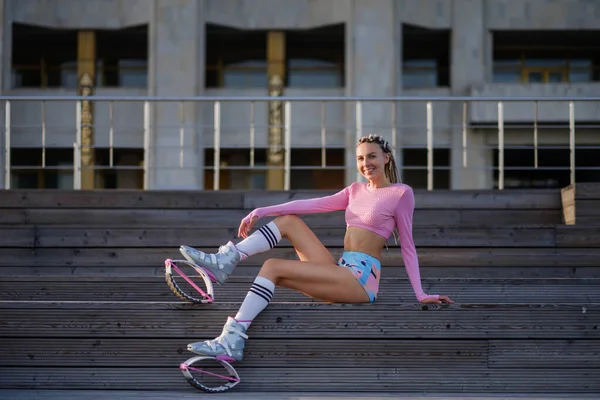 Junge schöne Sportlerin mit Dreadlocks, in heller Sportbekleidung. Das Mädchen treibt Sport auf dem städtischen Sportplatz. Kangoo springt. — Stockfoto