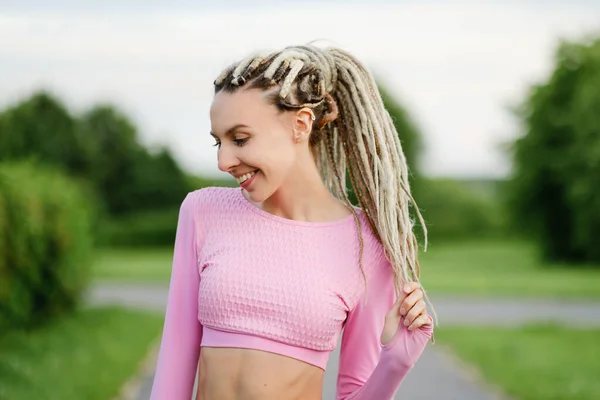 Eine junge schöne Frau in einem rosa T-Shirt mit weißen Dreadlocks im Freien. — Stockfoto