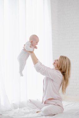 Beyaz tulumlu, yeni doğmuş bir bebeği elinde tutan beyaz elbiseli bir anne. Gülümsüyor ve çocuğa sarılıyor..