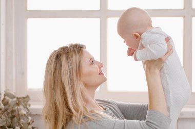 Genç, güzel, beyaz, sarışın anne bebeğiyle birlikte yatakta yatıyor. Beyaz ışıklı ev içi.