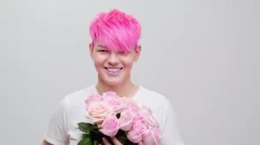 Kısa saçlı, pembe saçlı, güzel bir kız. Eşcinsel bir lezbiyen model beyaz arka planda poz veriyor. Kadın elinde pembe güller tutuyor..