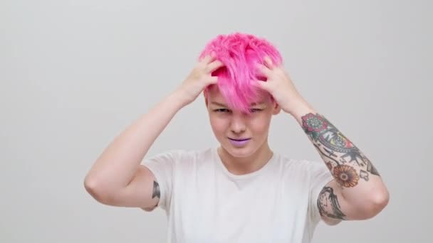 Joven chica hermosa con un corte de pelo corto y cabello rosa. Una modelo lesbiana homosexual posa sobre un fondo blanco. — Vídeos de Stock