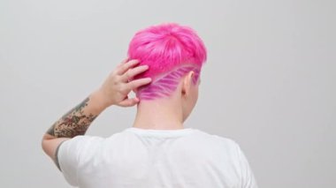 Kısa saçlı ve pembe saçlı güzel bir kız. Eşcinsel bir lezbiyen model beyaz bir arkaplanda poz veriyor..
