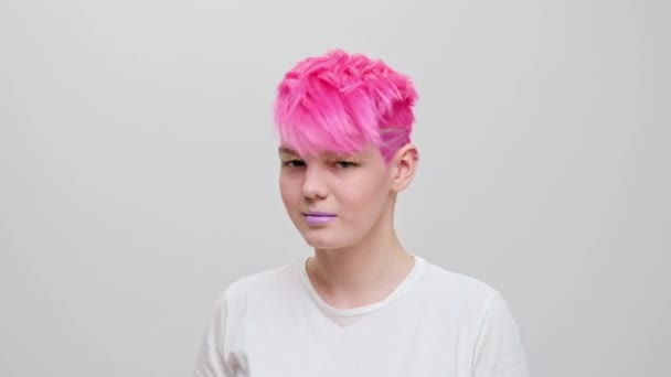 Joven chica hermosa con un corte de pelo corto y cabello rosa. Una modelo lesbiana homosexual posa sobre un fondo blanco. — Vídeos de Stock