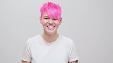 Kısa saçlı ve pembe saçlı güzel bir kız. Eşcinsel bir lezbiyen model beyaz bir arkaplanda poz veriyor..