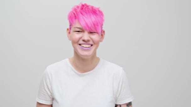 Joven chica hermosa con un corte de pelo corto y cabello rosa. Una modelo lesbiana homosexual posa sobre un fondo blanco. — Vídeos de Stock
