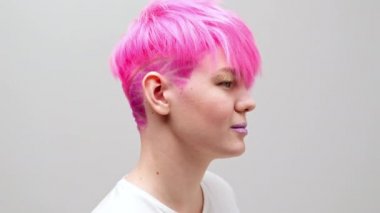 Kısa saçlı ve pembe saçlı güzel bir kız. Eşcinsel bir lezbiyen model beyaz bir arkaplanda poz veriyor..