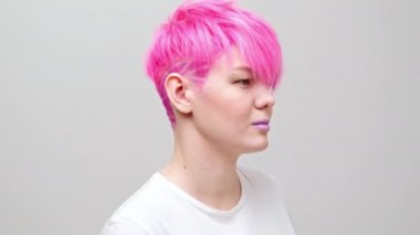 Kısa saçlı ve pembe saçlı güzel bir kız. Eşcinsel bir lezbiyen model beyaz bir arkaplanda poz veriyor..