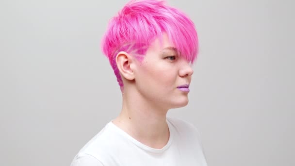 Joven chica hermosa con un corte de pelo corto y cabello rosa. Una modelo lesbiana homosexual posa sobre un fondo blanco. — Vídeos de Stock