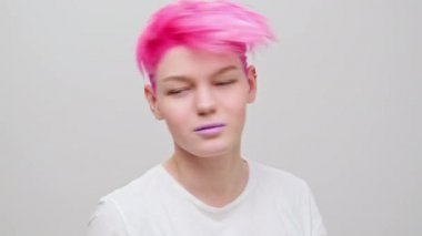Kısa saçlı ve pembe saçlı güzel bir kız. Eşcinsel bir lezbiyen model beyaz bir arkaplanda poz veriyor..