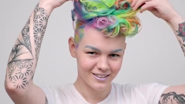 Una joven con un corte de pelo corto y bueyes pintados en los colores del arco iris. Teñido multicolor. Se posa sobre un fondo blanco. — Vídeos de Stock