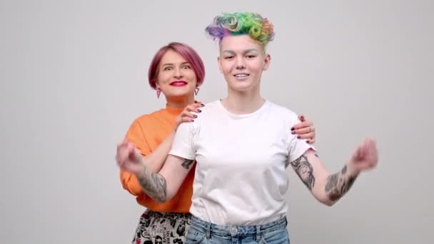 Due ragazze con capelli tinti di colore brillante e tagli di capelli corti. Colorista parrucchiere e modello posare su uno sfondo bianco. Coppia lesbica omosessuale. — Video Stock