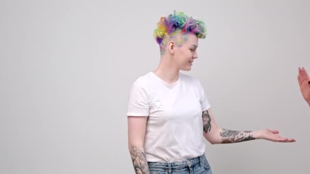 Two young girls with bright colored dyed hair and short haircuts. Hairdresser colorist and model pose against a white background. Homosexual lesbian couple. — Stock Video