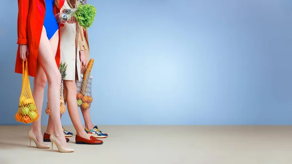 Drei junge modische Hausfrauen in roten und blauen Badeanzügen und Trenchcoats auf nacktem Körper. Shopper Streifen Taschen mit Lebensmitteln in den Händen. Einkaufen, Einkaufen und Konsumieren. Schöne lange Beine. — Stockfoto