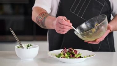 Erkek şef taze hazırlanmış salatayı sos veya tereyağıyla doldurur. Sosu cam kaseden bir kaşıkla döker. Restoranın mutfağında yemek pişirmek..