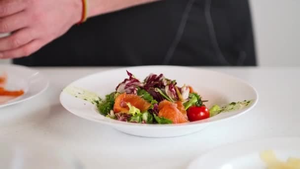 O chef masculino prepara uma salada de legumes e peixe vermelho na cozinha do restaurante. Close-up. — Vídeo de Stock