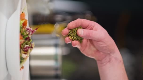 De mannelijke chef bereidt een salade van groenten en rode vis in de keuken van het restaurant. Bestrooit de salade met pompoenpitten. — Stockvideo