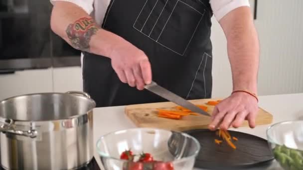 남자 요리사는 식당의 주방에서 야채 샐러드를 준비하는 앞치마의 전문가이다. 요리사는 도마에 칼을 꿰어 생당근을 자른다. — 비디오