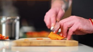 Bir erkek şef, restoranın mutfağında sebze salatası hazırlayan önlüklü bir profesyoneldir. Aşçı kesme tahtasındaki bir bıçakla çiğ havucu keser..