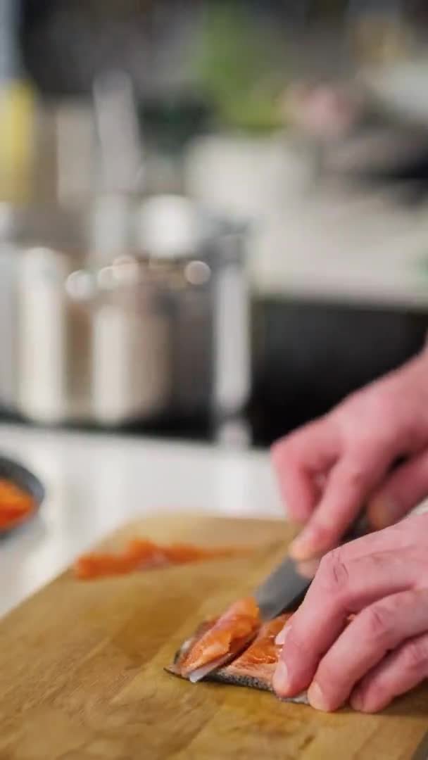 Чоловічий шеф-кухар розрізає червону рибу, лосось або форель ножем на дерев'яній обробній дошці на кухні ресторанів. приготування їжі . — стокове відео