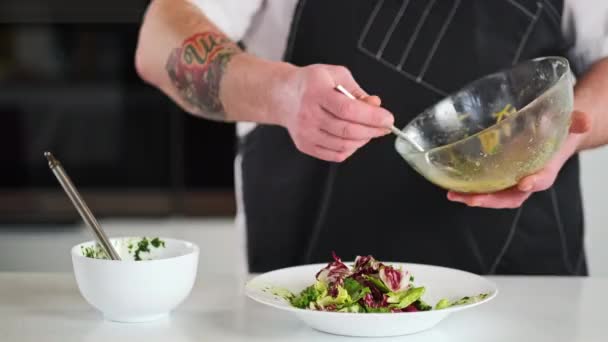 O chef masculino enche a salada com molho e manteiga. O cozinheiro adiciona o molho com uma colher de uma tigela de vidro. Cozinhar na cozinha do restaurante. — Vídeo de Stock