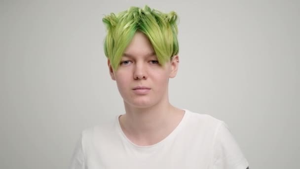 A young girl with a short pixie haircut and green hair in a white T-shirt on a light background. A woman poses in the studio, smiles and shows emotions. — Stock Video