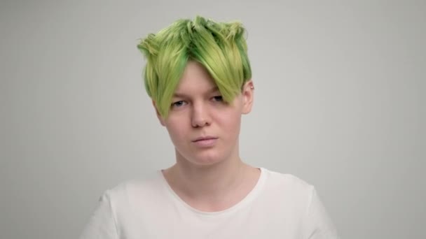 A young girl with a short pixie haircut and green hair in a white T-shirt on a light background. A woman poses in the studio, smiles and shows emotions. — Stock Video