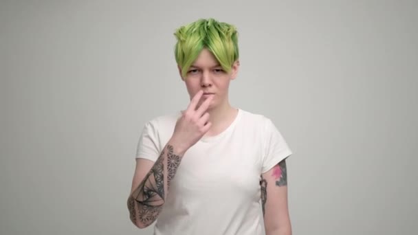 밝은 배경에 흰색 티셔츠를 입은 짧은 유화 헤어와 녹색 머리의 소녀. 한 여자 가 화실에서 웃으며 감정을 보여 주는 모습. — 비디오