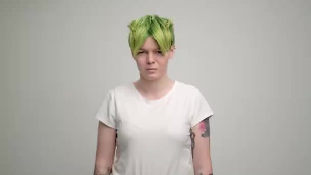 Egy fiatal lány rövid tündér frizurával és zöld hajjal fehér pólóban, világos háttérrel. Egy nő pózol a stúdióban, mosolyog és érzelmeket mutat.. — Stock videók