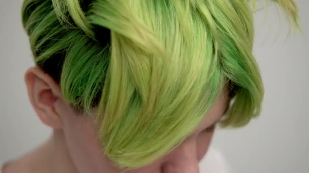 A young girl with a short pixie haircut and green hair in a white T-shirt on a light background. A woman poses in the studio, smiles and shows emotions. — Stock Video