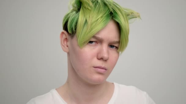 Seorang gadis muda dengan potongan rambut pixie pendek dan rambut hijau dengan kaos putih dengan latar belakang cahaya. Seorang wanita berpose di studio, tersenyum dan menunjukkan emosi. — Stok Video