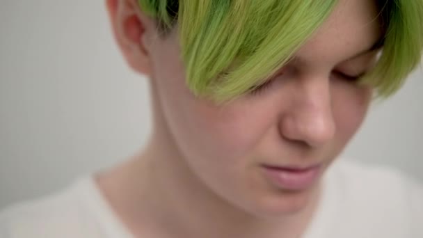 Kısa saçlı, yeşil saçlı, beyaz tişörtlü, açık arkaplanlı genç bir kız. Bir kadın stüdyoda poz veriyor, gülümsüyor ve duygularını gösteriyor.. — Stok video