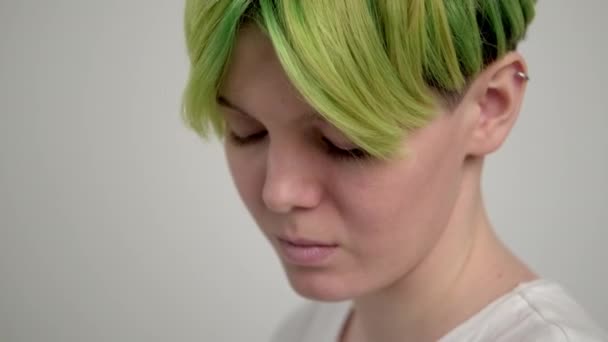 Une jeune fille avec une coupe de cheveux courte pixie et les cheveux verts dans un T-shirt blanc sur un fond clair. Une femme pose en studio, sourit et montre des émotions. — Video