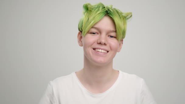 Uma jovem com um corte de cabelo curto pixie e cabelo verde em uma camiseta branca em um fundo claro. Uma mulher posa no estúdio, sorri e mostra emoções. — Vídeo de Stock