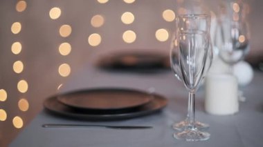 Şenlikli servis edilen yemek masası. Güzel yemekler, masa örtüleri, şarap bardakları ve gri tabaklar. Mumlar ve arka planda bir çelenk. Minimalist yemek odası dekorasyonu. Noel.