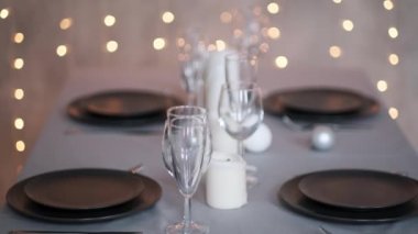 Şenlikli servis edilen yemek masası. Güzel yemekler, masa örtüleri, şarap bardakları ve gri tabaklar. Mumlar ve arka planda bir çelenk. Minimalist yemek odası dekorasyonu. Noel.