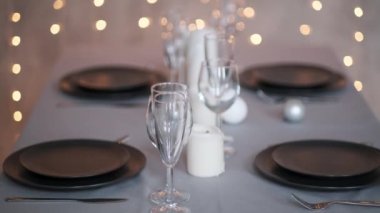 Şenlikli servis edilen yemek masası. Güzel yemekler, masa örtüleri, şarap bardakları ve gri tabaklar. Mumlar ve arka planda bir çelenk. Minimalist yemek odası dekorasyonu. Noel.