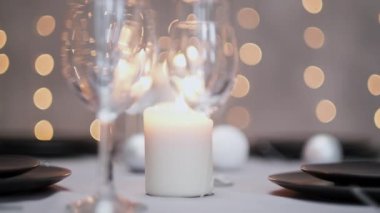 Şenlikli servis edilen yemek masası. Güzel yemekler, masa örtüleri, şarap bardakları ve gri tabaklar. Mumlar ve arka planda bir çelenk. Minimalist yemek odası dekorasyonu. Noel.