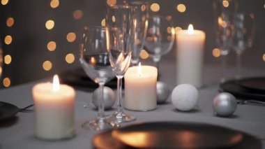 Şenlikli servis edilen yemek masası. Güzel yemekler, masa örtüleri, şarap bardakları ve gri tabaklar. Mumlar ve arka planda bir çelenk. Minimalist yemek odası dekorasyonu. Noel.