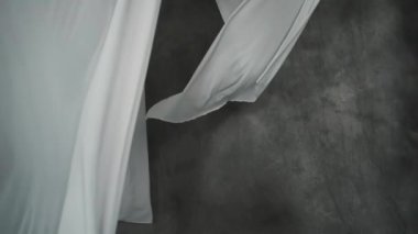 Beyaz kumaş çarşaflar ipteki mandallarla kurutulur. Dalgalı kumaş rüzgarda sallanıyor. Soyut gri arkaplan.