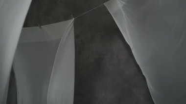 Beyaz kumaş çarşaflar ipteki mandallarla kurutulur. Dalgalı kumaş rüzgarda sallanıyor. Soyut gri arkaplan.