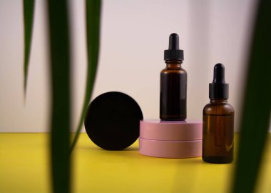 Bir kavanoz krema, bir şişe serum ve yeşil yapraklar.