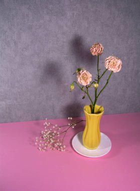 Beyaz bir tabakta sarı bir vazoda kurumuş güller..