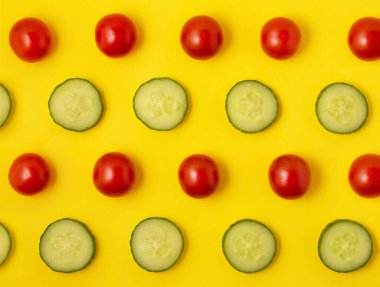 Parlak sarı arka planda kırmızı domates deseni ve yeşil salatalık dilimleri. Vejetaryen konsepti. Poster ve ambalaj için uygun. Düz yatış biçimi, üst görünüm