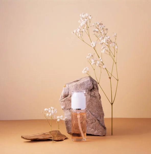 Garrafa cosmética com gel ou outro produto cosmético, pedras, flores de plantas secas e um pedaço de madeira em fundo bege. — Fotografia de Stock