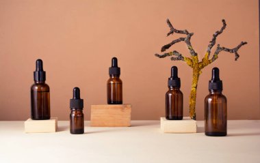 Ahşap podyumlarda bej arka planda serum için cam şişeler. Arka planda kuru bir ahşap dal var. Sıvı deri ya da saç bakım ürünü. Doğal kozmetik konsepti. Ön görünüm