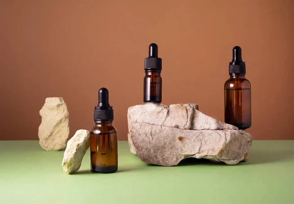 Serum and oil cosmetic bottles on concrete stone podium on brown and green background. Trendy natural organic healthy hair, face and body skin care