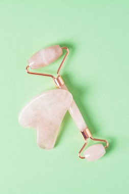 Yeşil arka planda paten ve gua sha yüz masajı aletleri. Cilt bakımı, güzellik ve sağlık konsepti